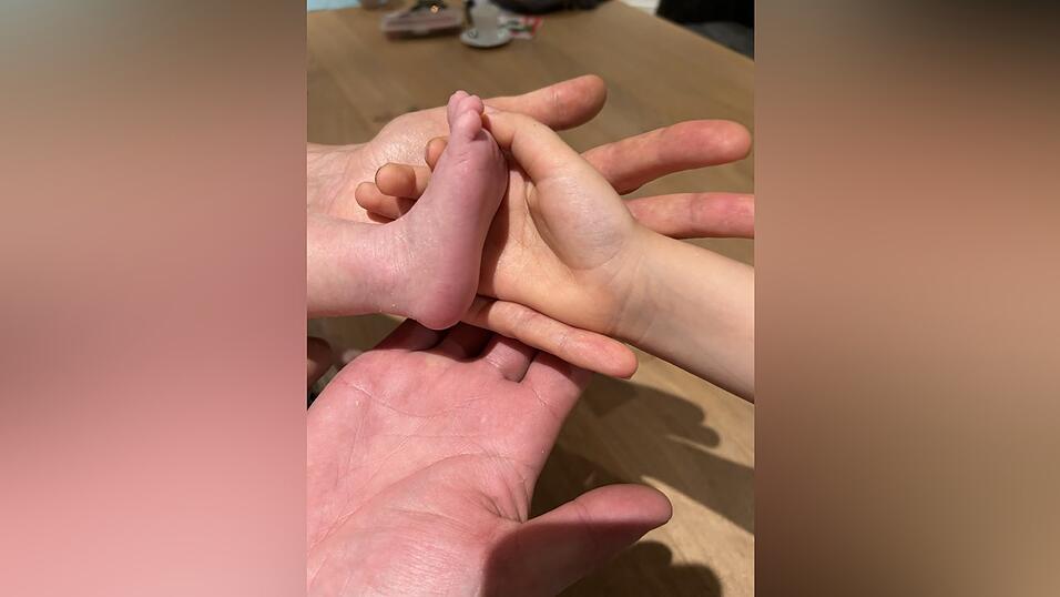 Z&auml;rtlich ber&uuml;hren die Eltern und ihre &auml;lteste Tochter den kleinen Fu&szlig; des Babys, das gesund zur Welt kommen durfte und nun viele Fu&szlig;abdr&uuml;cke in ihrem gemeinsamen Familienleben hinterlassen soll.