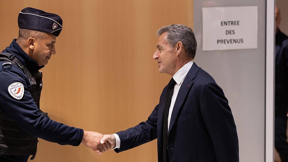 Beim Betreten des Gerichtssaals schüttelt der ehemalige französische Präsident Nicolas Sarkozy (r.) einem Polizeibeamten die Hand.