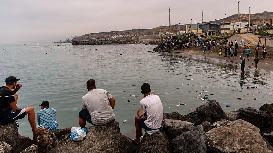 Migranten blickten von Felsen aus, w&auml;hrend andere aus der spanischen Enklave Ceuta nach Marokko zur&uuml;ckkehrten.