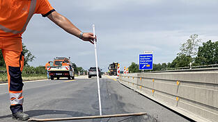 Ein Arbeiter verdeutlicht, wie stark die Absenkungen und W&ouml;lbungen auf dem Asphalt waren.