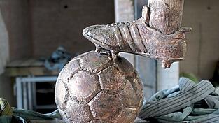 Der rechte Fuß ruht auf einem Fußball aus Bronze.