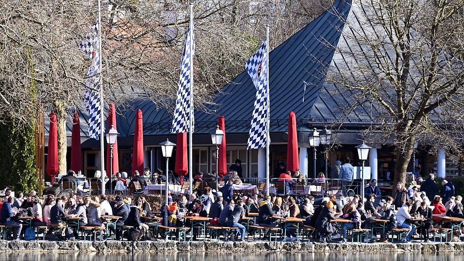 Zahlreiche Menschen sitzen in einem Biergarten im Englischen Garten am Kleinhesseloher See und genießen die Sonne. Zahlreiche Menschen sitzen in einem Biergarten im Englischen Garten am Kleinhesseloher See und genießen die Sonne.
