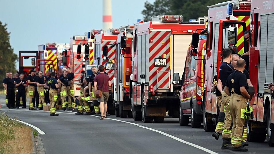Zahlreiche Kräfte der Feuerwehr stehen an einer Straße. Zahlreiche Kräfte der Feuerwehr stehen an einer Straße.