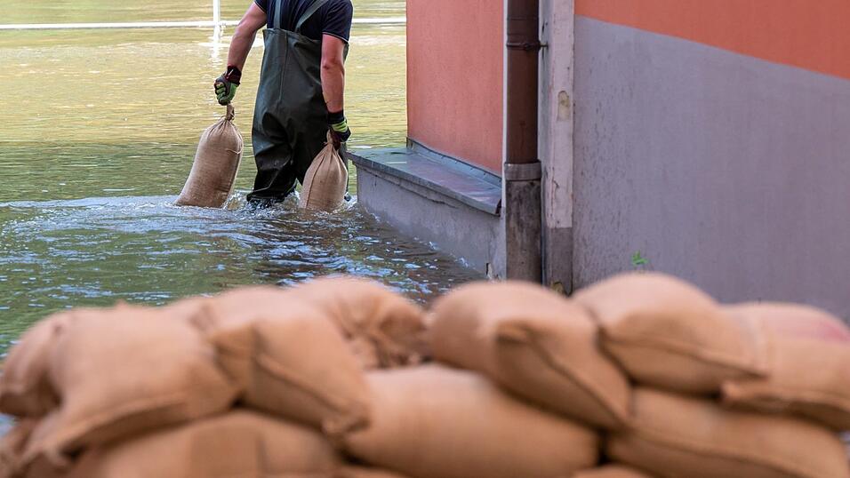 Ein Mann trägt Sandsäcke um Abdichten von Türen und Fenstern durch das Wasser der Donau, das auf der Uferpromenade der Stadt Passau steht. Ein Mann trägt Sandsäcke um Abdichten von Türen und Fenstern durch das Wasser der Donau, das auf der Uferpromenade der Stadt Passau steht.