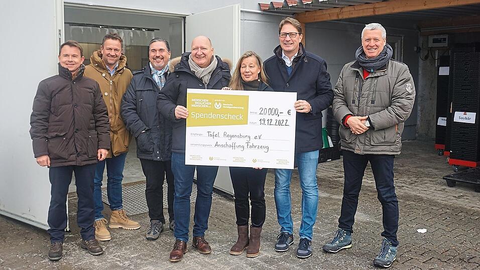 Den Scheck halten (v.l.) Stephan King (Allfinanz), Jonah Lindinger (Vorsitzende Tafel Regensburg) und Christopher Sitte (Verein Menschen brauchen Menschen), umringt von weiteren Vermögensberatern.