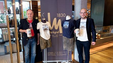 Festwirtesprecher Martin Lechner (l.) und Krug-Koordinator Festwirt Stefan Wenisch pr&auml;sentieren den diesj&auml;hrigen Krug, zu dem es auch passende T-Shirts gibt, und freuen sich auf Ma&szlig;-Krug-Ideen f&uuml;r 2027.