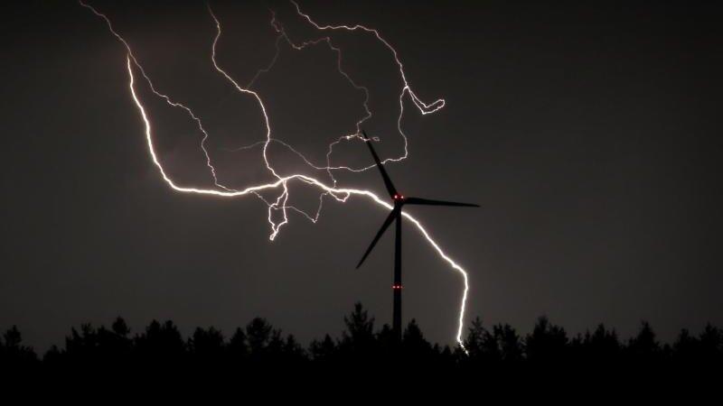 Blitze entladen sich hinter einem Windrad.
