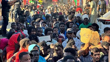 Migranten warten in einer Schlange auf Grundnahrungsmittel, die von Mitarbeitern des Roten Kreuzes und der Organisation &bdquo;Sur Sur&ldquo; verteilt werden.