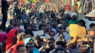 Migranten warten in einer Schlange auf Grundnahrungsmittel, die von Mitarbeitern des Roten Kreuzes und der Organisation „Sur Sur“ verteilt werden. Migranten warten in einer Schlange auf Grundnahrungsmittel, die von Mitarbeitern des Roten Kreuzes und der Organisation „Sur Sur“ verteilt werden.