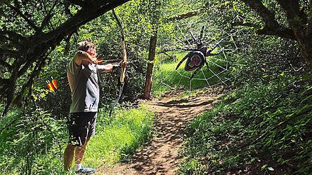 Ein Bogenschütze zielt im Schaumberger Bogensport-Parcours in Tholey im Saarland auf eine riesige Spinne in einem Netz. Ein Bogenschütze zielt im Schaumberger Bogensport-Parcours in Tholey im Saarland auf eine riesige Spinne in einem Netz.