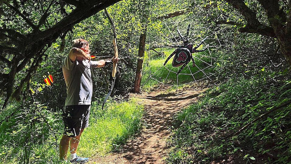 Ein Bogenschütze zielt im Schaumberger Bogensport-Parcours in Tholey im Saarland auf eine riesige Spinne in einem Netz. Ein Bogenschütze zielt im Schaumberger Bogensport-Parcours in Tholey im Saarland auf eine riesige Spinne in einem Netz.