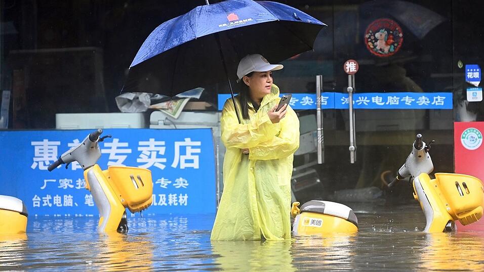 Eine Frau steht in Qinzhou auf einer mit Wasser vollgelaufenen Stra&szlig;e.