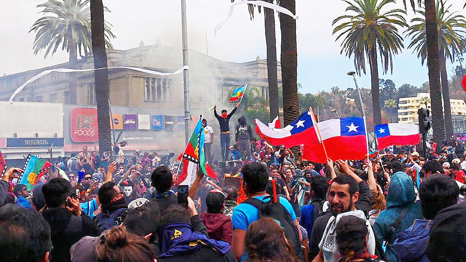 Über dem Plaza de Viña in Chile hängt eine Tränengaswolke, die Menschenmenge wirft Klopapierrollen in die Luft und schwenkt Chile-Flaggen.Die Proteste im Zentrum von Viña del Mar werden mit einem Wasserwerfer aufgelöst. Im Hintergrund eine Straßenblockade. Fotos: Bea Escherich Über dem Plaza de Viña in Chile hängt eine Tränengaswolke, die Menschenmenge wirft Klopapierrollen in die Luft und schwenkt Chile-Flaggen.Die Proteste im Zentrum von Viña del Mar werden mit einem Wasserwerfer aufgelöst. Im Hintergrund eine Straßenblockade. Fotos: Bea Escherich