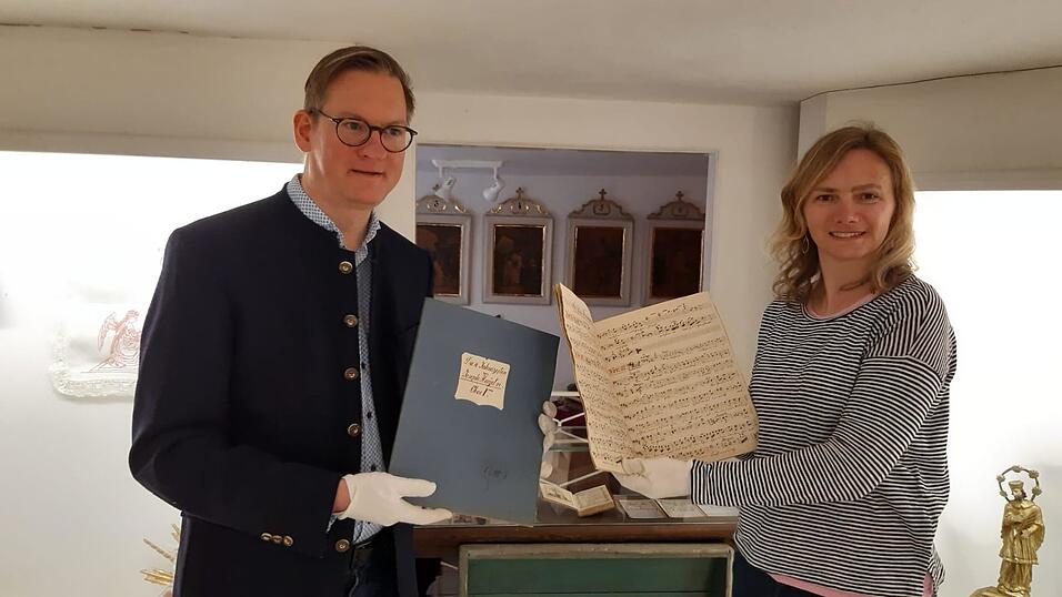 Nadine Ziska-Heindl und Martin Heindl mit den handgeschriebenen Noten von Johann Baptist und Joseph Oettl, dazwischen das handgeschriebene und handbemalte Gebetbuch von Johann Baptist Oettl.