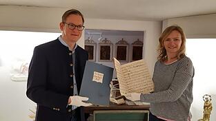 Nadine Ziska-Heindl und Martin Heindl mit den handgeschriebenen Noten von Johann Baptist und Joseph Oettl, dazwischen das handgeschriebene und handbemalte Gebetbuch von Johann Baptist Oettl.