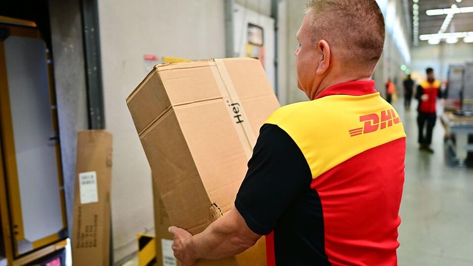 Ein Paketbote schleppt in einem DHL-Standort ein schweres Paket. (Archivbild) Ein Paketbote schleppt in einem DHL-Standort ein schweres Paket. (Archivbild)