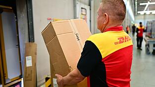 Ein Paketbote schleppt in einem DHL-Standort ein schweres Paket. (Archivbild) Ein Paketbote schleppt in einem DHL-Standort ein schweres Paket. (Archivbild)