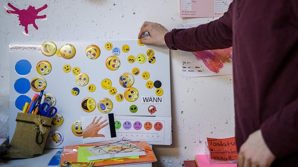 Ein junger Mann mit fr&uuml;hkindlichem Autismus heftet in seinem Therapiezimmer einen Smiley an eine Tafel. Sie stellen Superpunkte dar, mit denen er bestimmen kann, was er in seinen Therapiepausen machen m&ouml;chte.