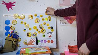 Ein junger Mann mit frühkindlichem Autismus heftet in seinem Therapiezimmer einen Smiley an eine Tafel. Sie stellen Superpunkte dar, mit denen er bestimmen kann, was er in seinen Therapiepausen machen möchte. Ein junger Mann mit frühkindlichem Autismus heftet in seinem Therapiezimmer einen Smiley an eine Tafel. Sie stellen Superpunkte dar, mit denen er bestimmen kann, was er in seinen Therapiepausen machen möchte.