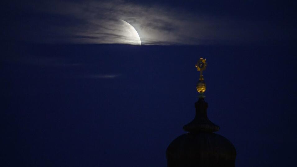 Der Mond geht am Morgen während einer partiellen Mondfinsternis hinter dem Kreuz der Frauenkirche unter. Der Mond geht am Morgen während einer partiellen Mondfinsternis hinter dem Kreuz der Frauenkirche unter.