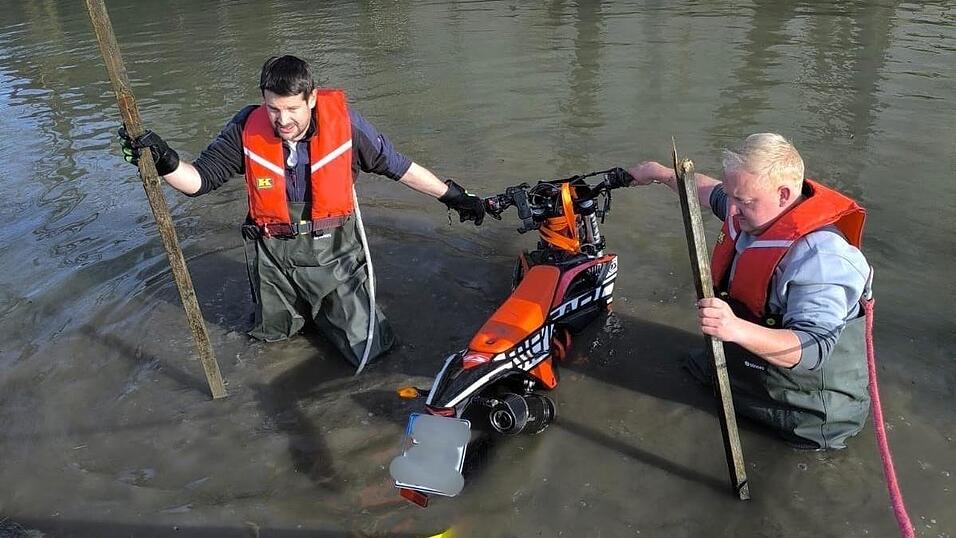 Zwei Feuerwehrleute aus Ro&szlig;bach bergen das Leichtkraftrad aus dem Wasser.