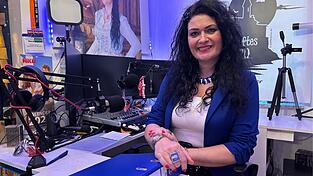 Christl Fischer sitzt in ihrem Studio, in dem sie ihre Radiosendung moderiert. Ihr gro&szlig;er Ring und die Sakkofarben verraten die Partei: Fischer ist die AfD-Landratskandidatin.