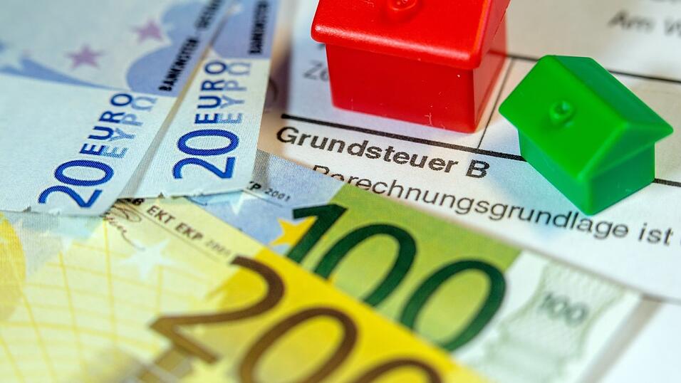 Ein Spielzeughaus und die Nachbildung von Euro-Geldscheinen liegen auf einem Abgabenbescheid f&uuml;r die Entrichtung der Grundsteuer.