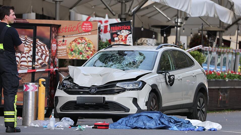 Rettungskr&auml;fte stehen in der N&auml;he eines besch&auml;digten Autos an der Stelle, wo ein Auto in eine Menschengruppe gefahren ist.