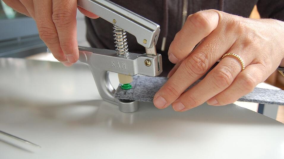 5. Dann ab damit unter die Druckknopfzange und fest zusammendrücken. Daneben das gleiche Spiel. Auf der gegenüberliegenden Seite dann wieder das Raster einzeichnen, Loch vorstechen und Druckknopf mit Nagel durchstecken. Beim Aufsetzen des Innenteils musst du aufpassen, dass du diesmal das richtige erwischt. Es gibt nämlich zwei unterschiedliche Innenteile, quasi zwei Gegenstücke, die ineinander passen. Schau einfach, welches du auf der anderen Seite verwendet hast und nimm dann das entsprechend andere. 5. Dann ab damit unter die Druckknopfzange und fest zusammendrücken. Daneben das gleiche Spiel. Auf der gegenüberliegenden Seite dann wieder das Raster einzeichnen, Loch vorstechen und Druckknopf mit Nagel durchstecken. Beim Aufsetzen des Innenteils musst du aufpassen, dass du diesmal das richtige erwischt. Es gibt nämlich zwei unterschiedliche Innenteile, quasi zwei Gegenstücke, die ineinander passen. Schau einfach, welches du auf der anderen Seite verwendet hast und nimm dann das entsprechend andere.