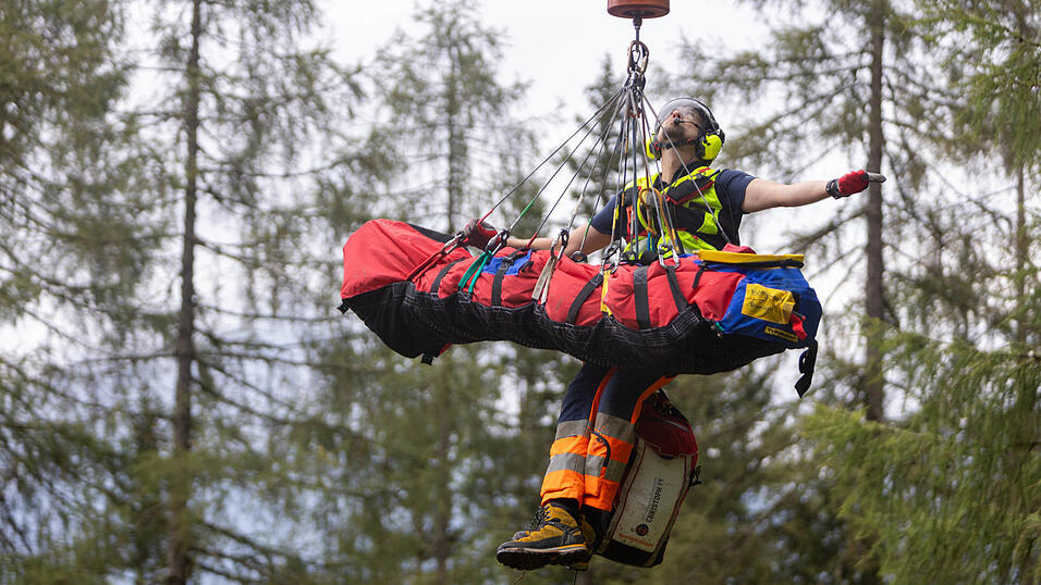 Jetzt muss es schnell gehen: In dieser Szene aus der Doku In höchster Not hat sich ein Bergretter der Bergwacht Ramsau mit einem Verletzten an die Rettungswinde des Hubschraubers gehängt. Gemeinsam bringen sie den Patienten aus der Gefahrensituation.
