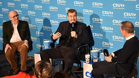 Ministerpr&auml;sident Markus S&ouml;der (Mitte) spricht vor einem vollen Saal &uuml;ber pers&ouml;nliche Erlebnisse. Landrat Martin Neumeyer (links) und Moderator Ralf Exel (rechts) begleiten ihn dabei.