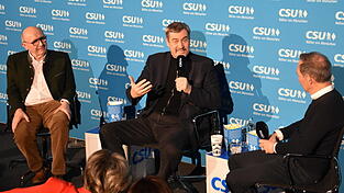 Ministerpräsident Markus Söder (Mitte) spricht vor einem vollen Saal über persönliche Erlebnisse. Landrat Martin Neumeyer (links) und Moderator Ralf Exel (rechts) begleiten ihn dabei. Ministerpräsident Markus Söder (Mitte) spricht vor einem vollen Saal über persönliche Erlebnisse. Landrat Martin Neumeyer (links) und Moderator Ralf Exel (rechts) begleiten ihn dabei.