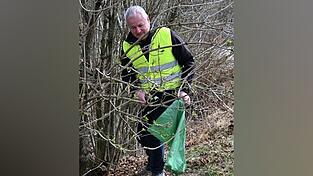 Bürgermeister Anton Piermeier sammelt im Gebüsch Pfandflaschen auf.