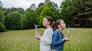 Zwei M&auml;dchen halten ein Modell einer Windkraftanlage und pusten. In Schierling geht der Windkraft die Puste aus.