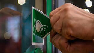 Ein Mitarbeiter der Magdeburger Verkehrsbetriebe (MVB) entfernt einen Aufkleber von der T&uuml;r einer Stra&szlig;enbahn, der auf die Pflicht zum Tragen einer Maske hinweist. Doch selbst, wenn sich die Corona-Lage entspannt hat: Das Virus ist keineswegs harmlos, sondern sorgt noch immer f&uuml;r schwere Verl&auml;ufe, Long Covid und auch f&uuml;r Todesf&auml;lle.