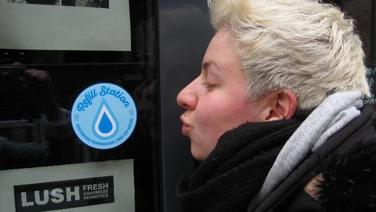 Louisa Bahl ist Sprecherin des Organisationsteams von 'Refill'. Der blaue Aufkleber zeigt, dass dieses Geschäft Teil des Projekts ist.