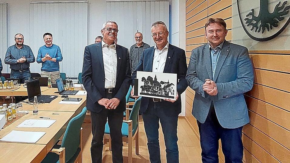 Mit stehenden Ovationen verabschieden die Stadtr&auml;te B&uuml;rgermeister Markus Ackermann; seine beiden Stellvertreter Martin Frank und Wolfgang K&uuml;rzinger, zugleich sein Nachfolger im Amt, &uuml;berreichen ihm einen Scherenschnitt.