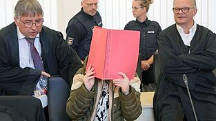 Die Angeklagte sitzt mit Aktendeckel vor dem Gesicht zwischen ihren Verteidigern Andreas Ohm (l-r) und Thomas L&ouml;cker.