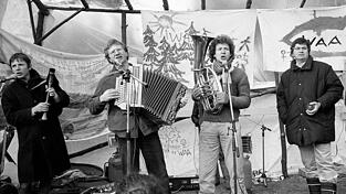 Die Bierm&ouml;sl Blosn (Christoph Well, Hans Well, Michael Well) und Gerhard Polt (rechts) demonstrieren am 5. Januar 1986 musizierend im H&uuml;ttendorf &bdquo;Freie Republik Wackerland&ldquo; gegen die Wiederaufbereitungsanlage Wackersdorf. Zwei Tage sp&auml;ter wurde das H&uuml;ttendorf von der Polizei ger&auml;umt.