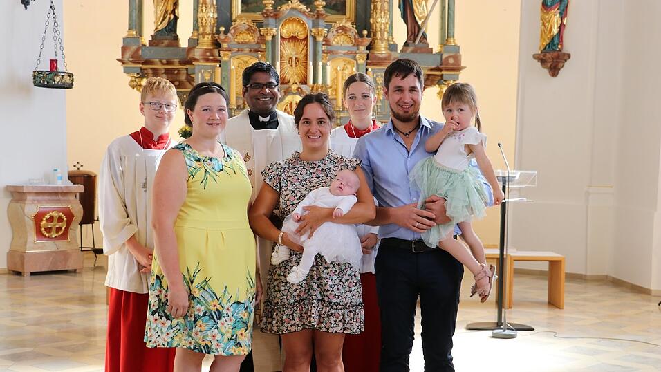 Täufling Magdalena Eckl auf dem Arm ihrer Patin und zusammen mit ihren Eltern, Schwester Johanna sowie Taufspender Pater Joseph und den Ministranten