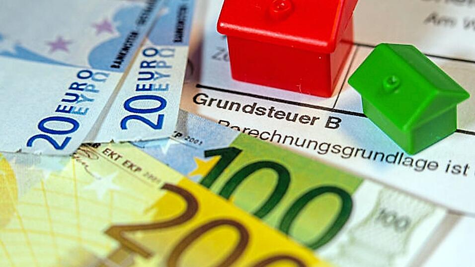 Ein Spielzeughaus und die Nachbildung von Euro-Geldscheinen liegen auf einem Abgabenbescheid f&uuml;r die Entrichtung der Grundsteuer. Der Stadtrat hat jetzt eine Entscheidung &uuml;ber die Straubinger Hebes&auml;tze ab 2025 getroffen.