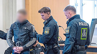 Die Finger ineinander verschr&auml;nkt, die H&auml;nde in Handschellen an einem Bauchgurt befestigt. Unter hohen Sicherheitsvorkehrungen bringen Polizisten einen der Angeklagten in den Verhandlungssaal.