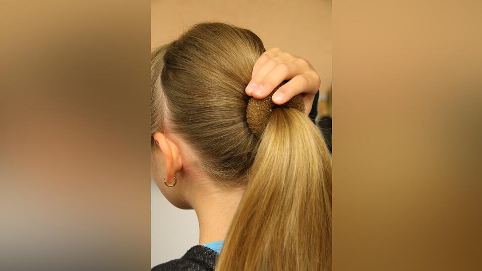 2. Dann schiebt sie ein Duttkissen &uuml;ber den Pferdeschwanz und toupiert ihre Haare leicht an.