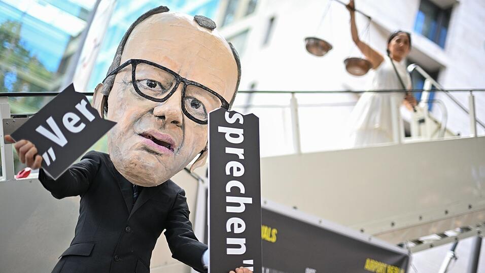 Ein Aktivist mit Merz-Maske zerbricht w&auml;hrend einer symbolischen Protestaktion von Kabul Luftbr&uuml;cke und Campact zur Unterst&uuml;tzung von Klagen von Afghanen gegen die Bundesregierung vor dem Ausw&auml;rtigen Amt ein Schild mit der Aufschrift &bdquo;Versprechen&ldquo;.