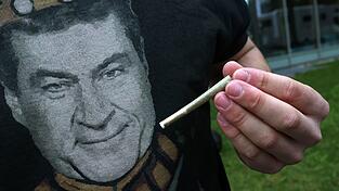 Ein Teilnehmer einer Versammlung, die unter dem Motto «Liberalitas Bavariae statt CSU-Verbotsirrtum» angemeldet wurde, hält am Gebäude der CSU-Landesleitung vor einem T-Shirt mit einem Portrait des bayerischen Ministerpräsidenten Markus Söder (CSU), einen Joint. Ein Teilnehmer einer Versammlung, die unter dem Motto «Liberalitas Bavariae statt CSU-Verbotsirrtum» angemeldet wurde, hält am Gebäude der CSU-Landesleitung vor einem T-Shirt mit einem Portrait des bayerischen Ministerpräsidenten Markus Söder (CSU), einen Joint.