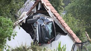 Ein Auto liegt nach einem kurzen Flug seitlich in der Mauer einer Scheune.