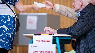 Eine Wahlhelferin gibt einen Stimmzettel aus. Landesweit fällt die Wahlbeteiligung unterschiedlich aus.