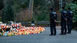 Mehrere Polizisten stehen vor der Ansammlung an Kerzen, Blumen und Kuscheltieren im Park.