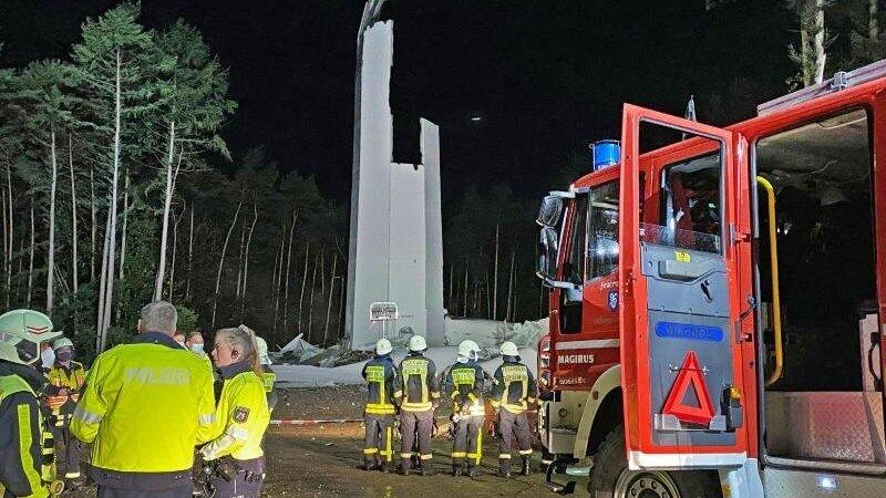 Feuerwehrleute und Polizisten stehen vor den Resten des Turms einer Windenergieanlage. Das fast 240 Meter hohe Windrad ist in sich zusammengest&uuml;rzt.