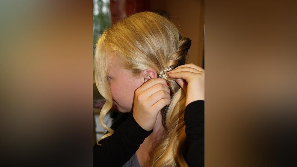 3. Am Ende fixiert sie die Kordel zusammen mit den restlichen Haaren mit einem Haargummi und frischt das Ganze mit einer Haarnadel mit Blume auf.